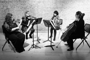Four musicians sit playing orchestral instruments